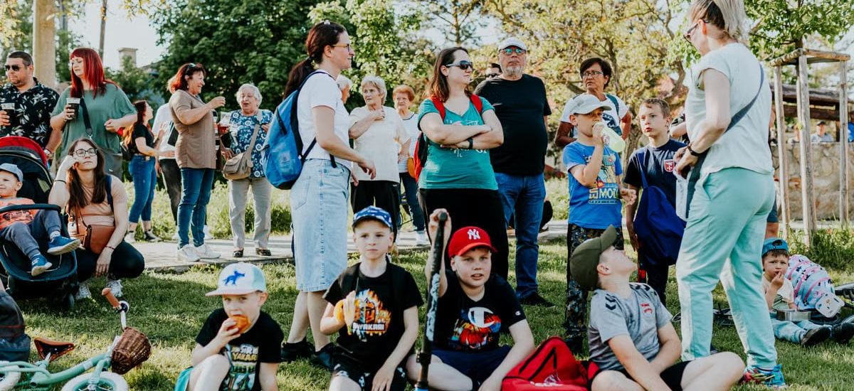 A diverse group of families and children enjoying an outdoor event on a sunny day in a park setting.